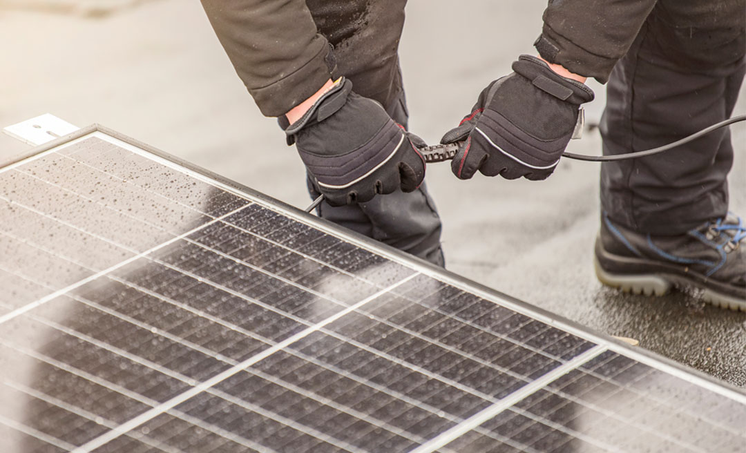 a person in gloves holding a cable to a solar panel