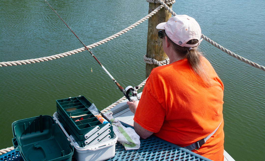a woman in an orange shirt holding a fishing pole